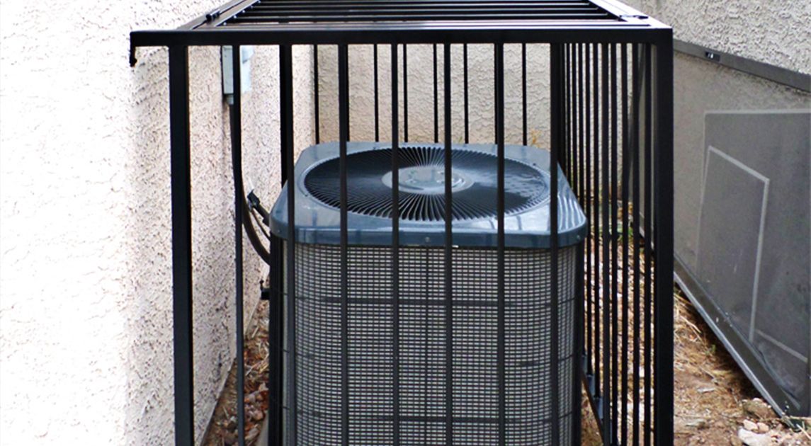 A wrought iron security cage surrounds a gray AC unit outdoors.