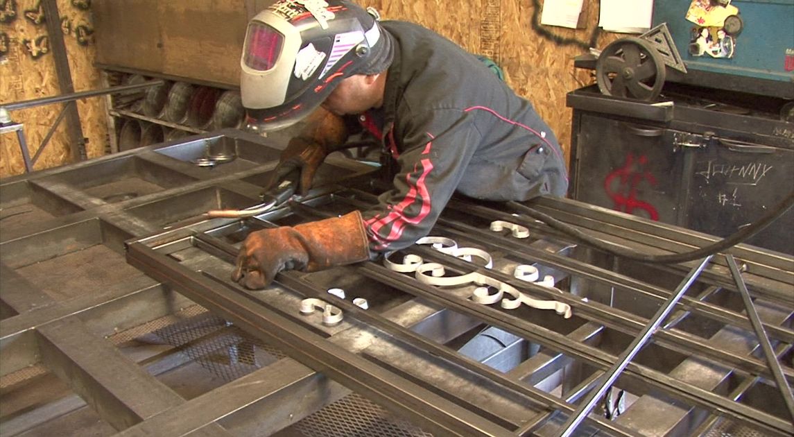 Craftsman leaning over wrought iron custom door doing welding work.